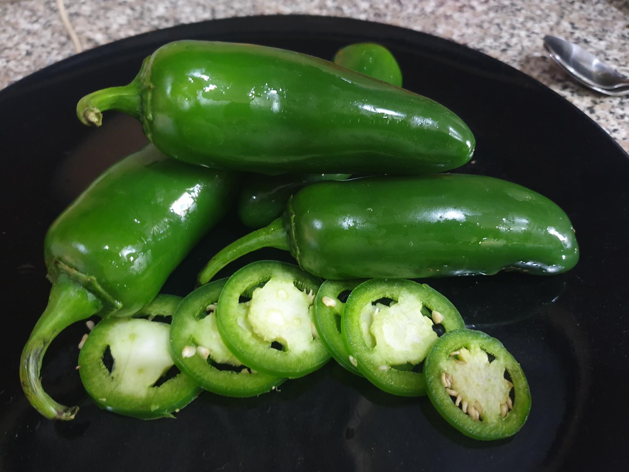 Fresh green jalapeños, whole and sliced, on a black plate