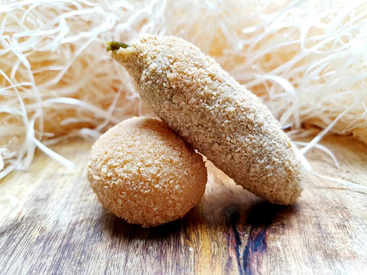 A golden crumbed jalapeño popper resting on a crumbed jalapeño cheese ball, on a wooden board with straw